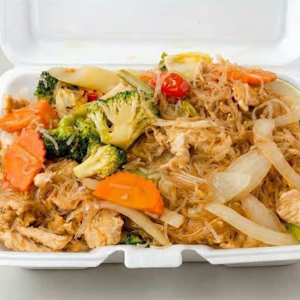 Glass noodles with chicken, broccoli, carrots, onions, and tomatoes in a white takeout container.
